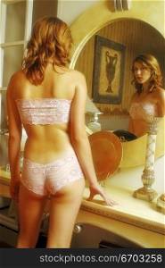 A sexy model looks at her body in a mirror.