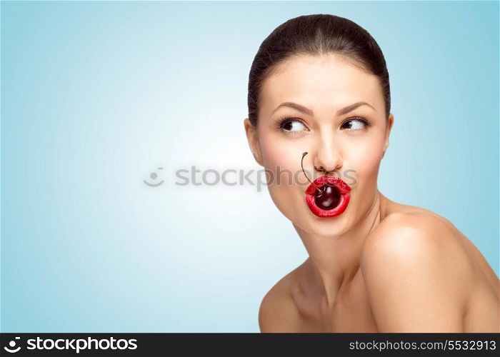 A sexy nude brunette holding a bright tempting cherry in her seductive mouth.