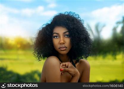 A sexy young black female with long black curly hair   beautiful makeup posing by herself in tropical surroundings.