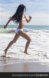 A sexy young brunette Asian woman or girl wearing a white bikini running on a deserted tropical beach with a blue sky