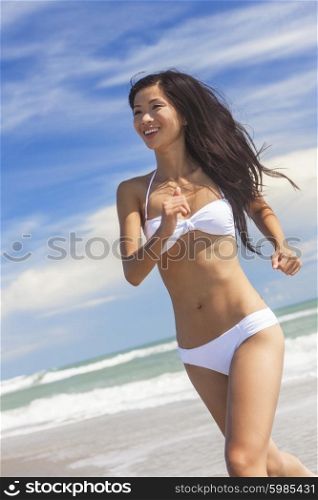 A sexy young brunette Asian woman or girl wearing a white bikini running on a deserted tropical beach with a blue sky