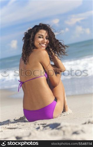 A sexy young brunette woman or girl wearing a bikini sitting on a deserted tropical beach with a blue sky