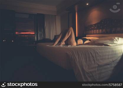 A sexy young woman in a swimsuit is lying on a hotel room bed at sunset