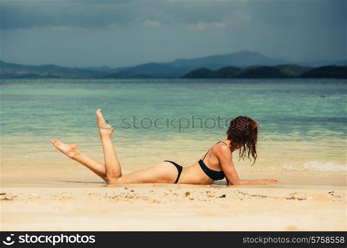A sexy young woman wearing a bikini is lying and posing on a tropical beach