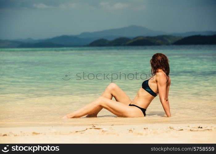 A sexy young woman wearing a bikini is lying and posing on a tropical beach