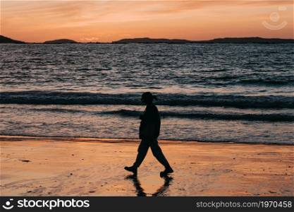 A shadow of a woman walking in front of a beach during a sunset