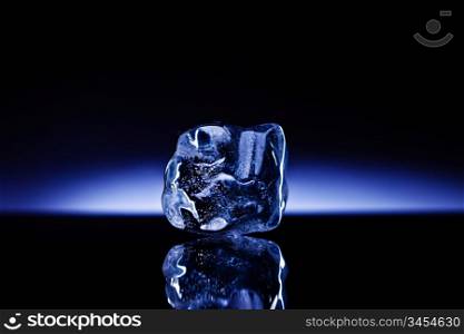 A shapeless piece of ice on reflective surface against the deep blue glowing background.