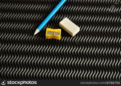 A sharpener, eraser and a blue writing pencil isolated on a black background