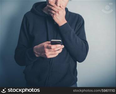 A shocked young man is using a smartphone and is covering his mouth with his hand