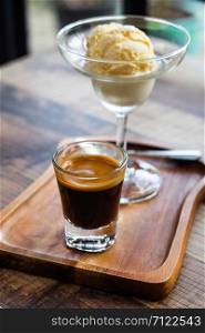A shot glass of hot espresso coffee served with vanilla ice cream call &rsquo; Affogato &rsquo; italian style dessert on wooden table in coffee shop, selective focus.