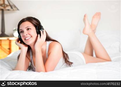 A shot of a beautiful girl lying down on the bed listening to music