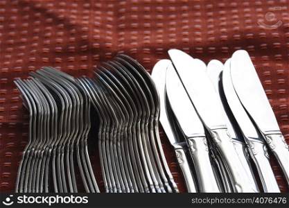 A shot of a bunch of knives and forks on a red tablecloth