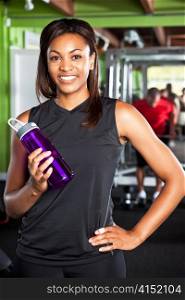A shot of a happy black female athlete holding a water bottle in a gym