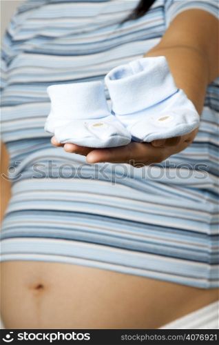 A shot of a pregnant woman showing baby shoes
