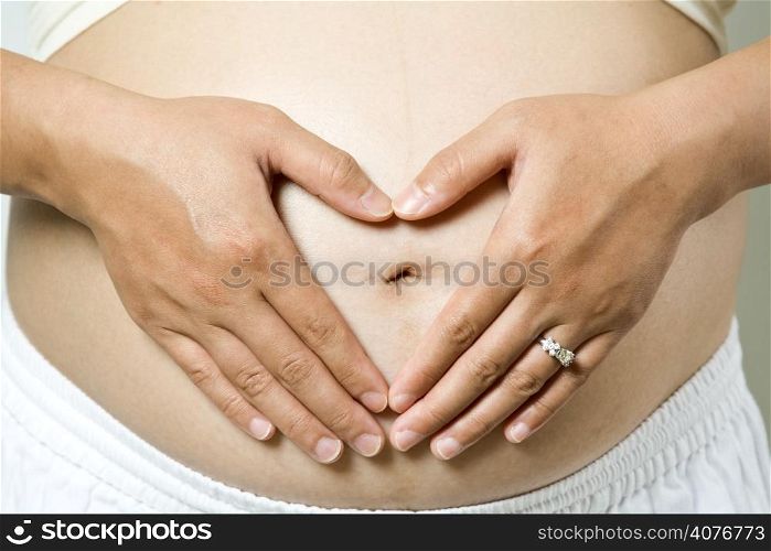 A shot of a pregnant woman with her hands forming a heart symbol for love