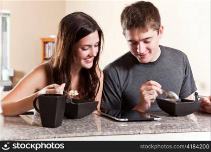A shot of a young couple eating breakfast and reading on tablet PC