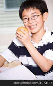 A shot of an asian kid studying and eating an apple at home