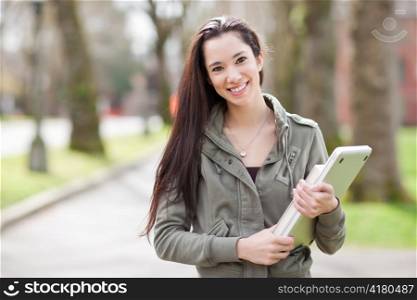 A shot of an ethnic college student carrying a book and a laptop on campus