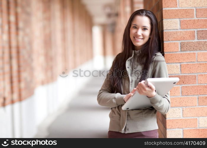 A shot of an ethnic college student carrying a laptop on campus