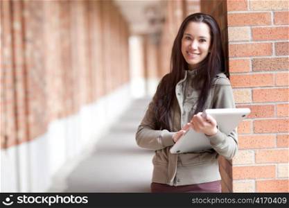 A shot of an ethnic college student carrying a laptop on campus