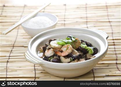 A shot of seafood casserole with a bowl of rice on a bamboo mat