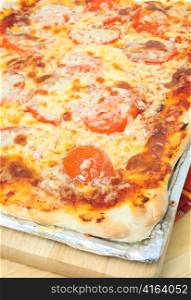 A Sicilian rectangular pizza with cheese and tomato topping on a baking sheet, the traditional way of serving the Sicilian type.