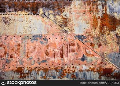 A side panel of an old railroad car is covered with rust, peeling paint, and old rivets in a post-industrial abstract background.