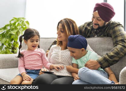 A SIKH BOY LOOKING AT MOBILE PHONE WITH FATHER AND MOTHER HAPPILY LOOKING AT HIS SISTER TALKING 