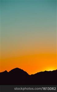 A silhouette of a mountain in black with a sunset sky gradient in orange and blue