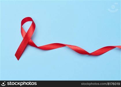 A silk red ribbon in the form of a bow is isolated on a blue background, a symbol of the fight against AIDS and a sign of solidarity and support