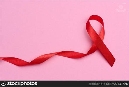 A silk red ribbon in the form of a bow on a pink background, a symbol of the fight against AIDS and a sign of solidarity and support