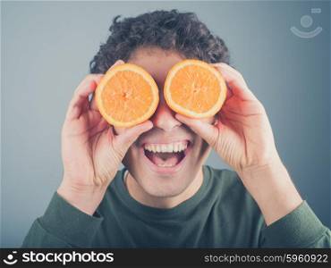 A silly young man is pretending to use two orange halves as binoculars