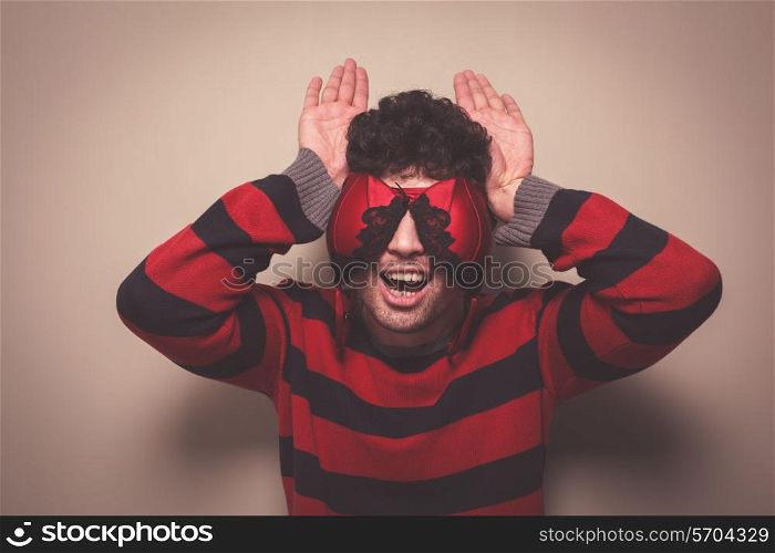 A silly young man wearing a bra on his face is making donkey ears with his hands