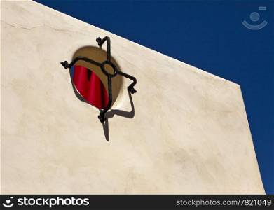 A simple architectural abstract based on the interplay between a white stucco wall with a few cracks, a deep blue sky, and a bright red umbrella.