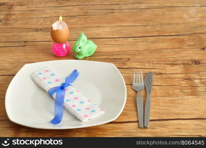 A simple easter place setting consisting of a plate, knife, fork and dot napkin tied with a blue ribbon and some easter table decorations.