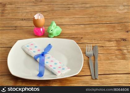 A simple easter place setting consisting of a plate, knife, fork and dot napkin tied with a blue ribbon and some easter table decorations.