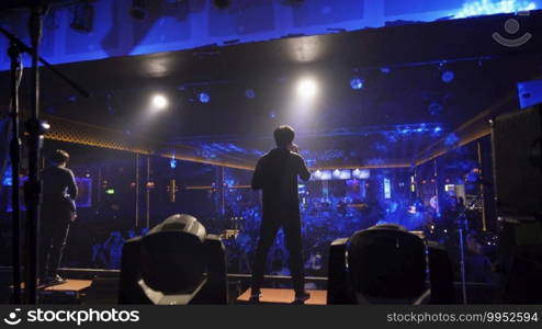 A singer with music band performing on a stage concert with lighting laser beam spotlight show in disco pub club bar for party music dancing festival performance. Entertainment nightlife. People.