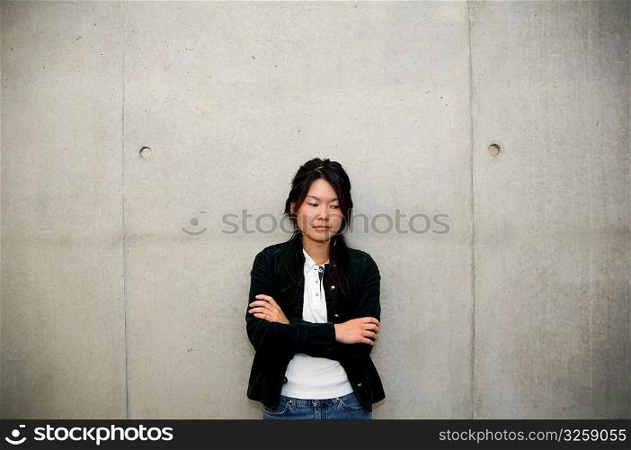 A single asian woman standing against cement wall.