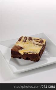 A single cream cheese brownie square shot in the studio on a white plate.