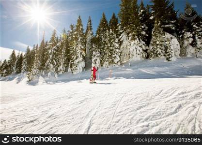 A single girl enjoys a sunny winter day of skiing, dressed in full snow gear with ski boots and sunglasses