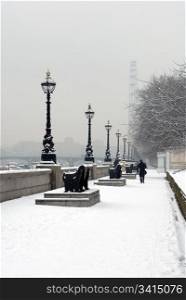 A single pedestrian walking in the snow beside the River Thames, London, England
