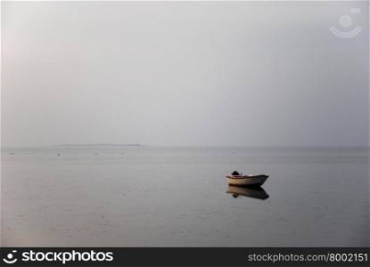 A single rowing boat in the water by a misty coast