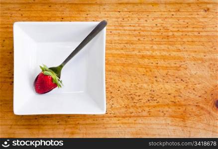 A single strawberry in a white contemporary bowl on wooden background