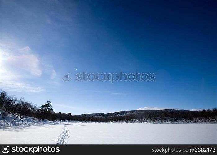 A ski trail going accross a frozen lake infront of a mountain landscape