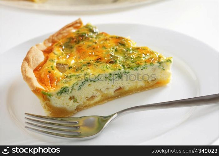 A slice of homemade cheese, onion and parsley quiche with a fork on a plate
