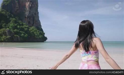 A slim fit asian girl doing slow full turn happily by the beach on her long holiday, tropical exotic beach to the ocean, summer vacation or holiday, huge natural mountain and ocean view on background