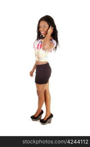 A slim young black woman standing in the studio for white backgroundin a short black skirt and colorful blouse showing her nice figure.