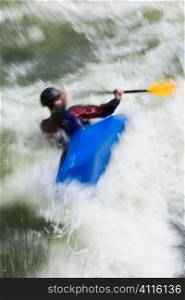 A slow shutterspeed shot of a kayaker capsizing in very rough whitewater.