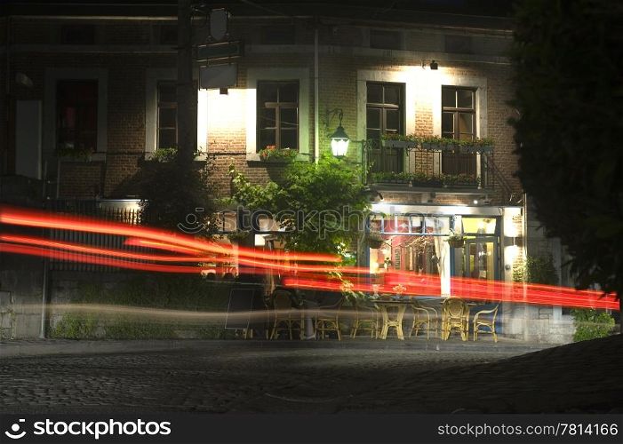 A small and cosy bar in an old village, with cars driving past over the cobblestone street at night