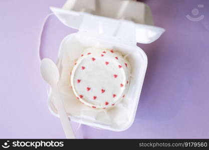 A small bento cake without an inscription in eco packaging with a wooden spoon on a purple background. A small bento cake in eco packaging with a wooden spoon on a purple background